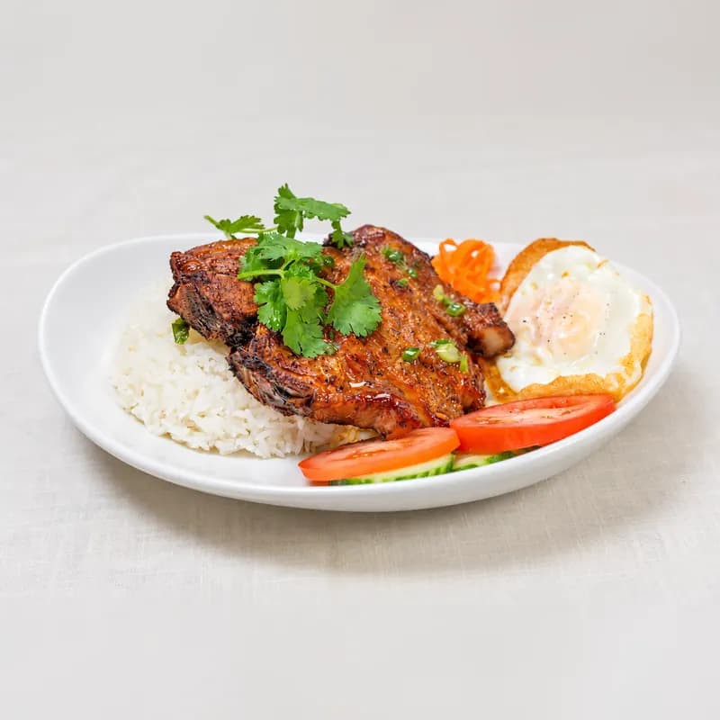Grilled pork chop over jasmine rice with a fried egg, tomato and cucumber
