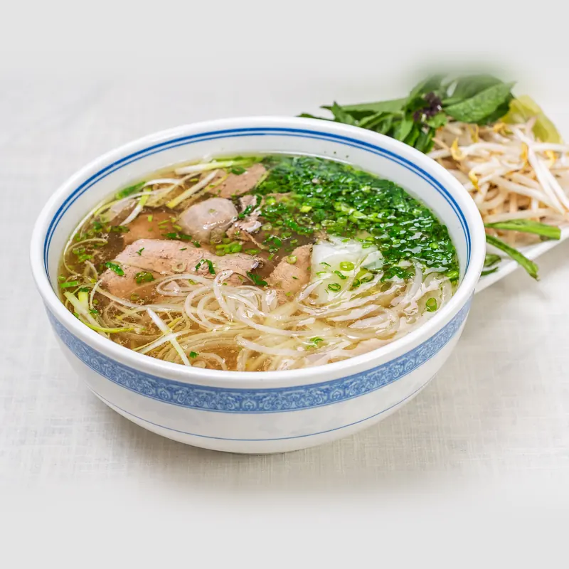 Steak and meatball phở with rice noodles, onion and cilantro in a blue-rimmed bowl